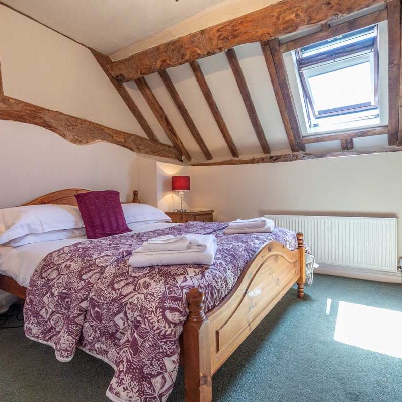Cozy attic bedroom with wooden beams, skylight, and a double bed.