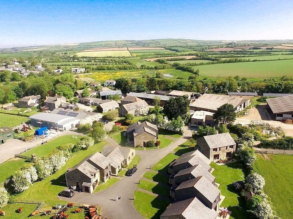 Aerial view of a rural village with farm buildings, houses, green fields, and countryside landscape.