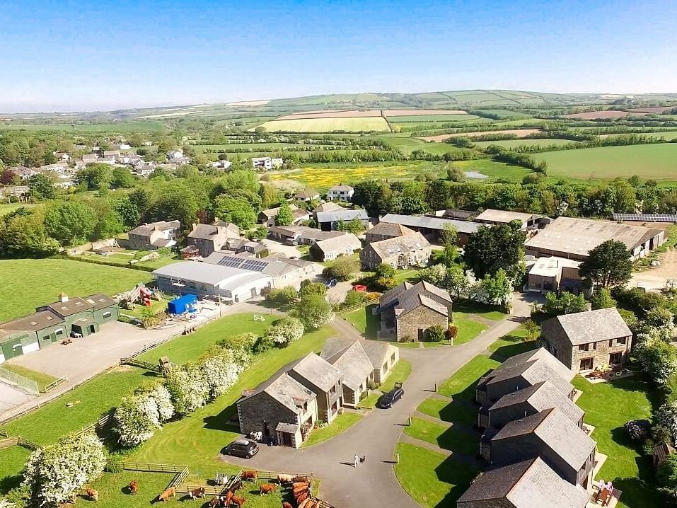 Aerial view of a rural village with farm buildings, houses, green fields, and countryside landscape.