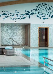 Indoor swimming pool with lounge chairs, a mosaic tile wall, and a fish mural above