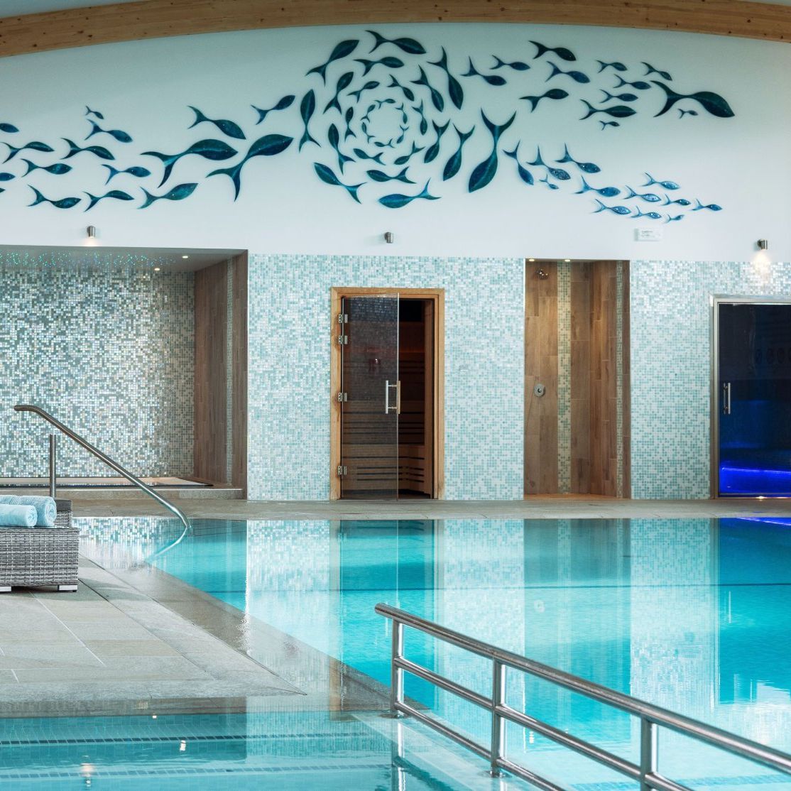Indoor swimming pool with lounge chairs, a mosaic tile wall, and a fish mural above