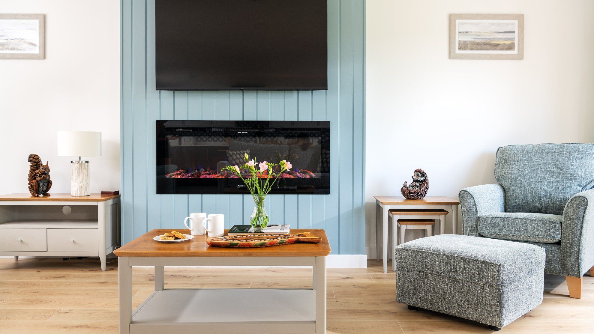 Modern living room with light blue accent wall, electric fireplace, TV, and cozy armchair