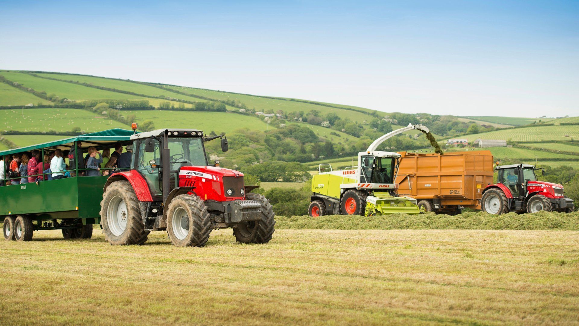 Tractors working in a field with one pulling a wagon full of people and another collecting harvested crops.