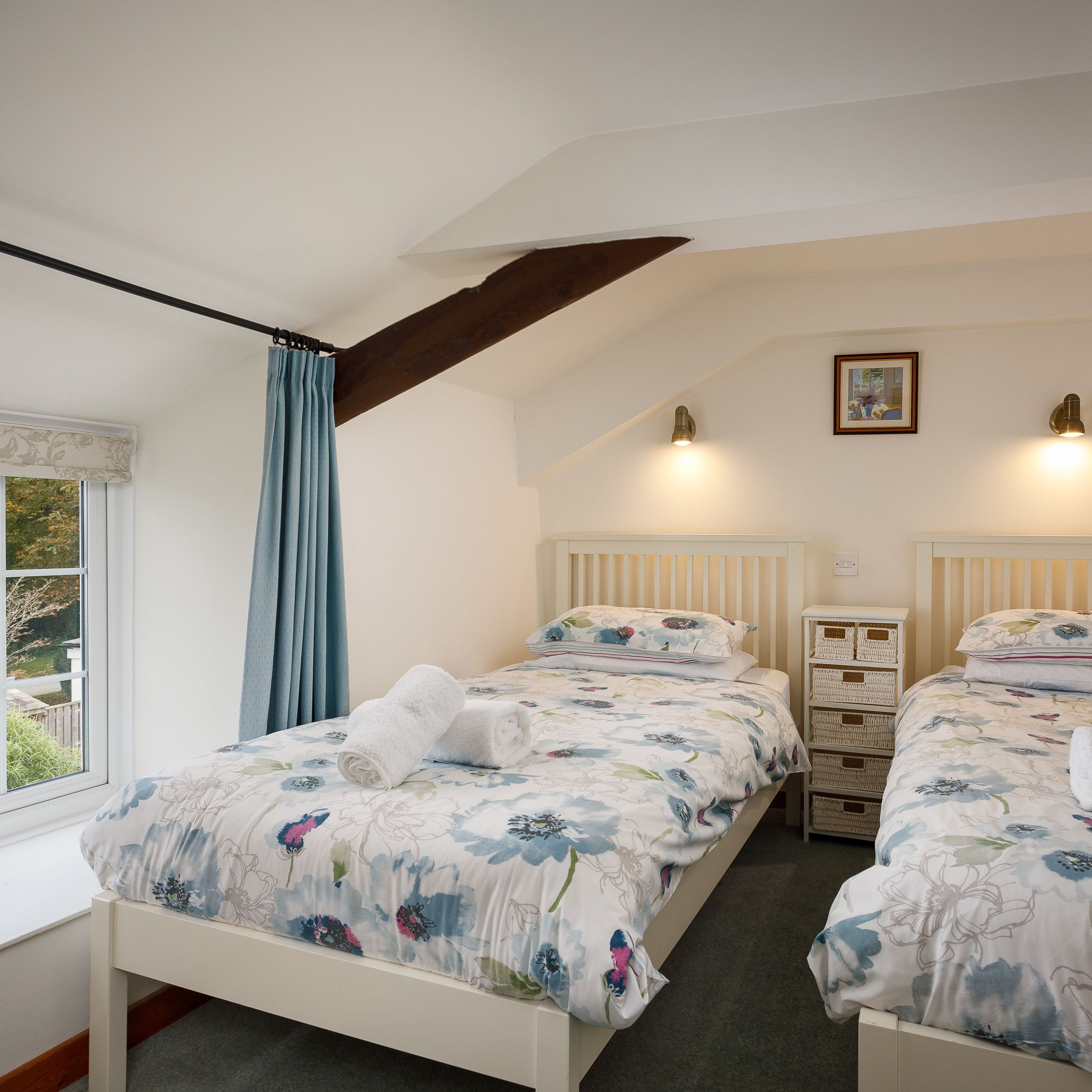 Twin bedroom with two single beds, floral bedding, and a window with a countryside view.