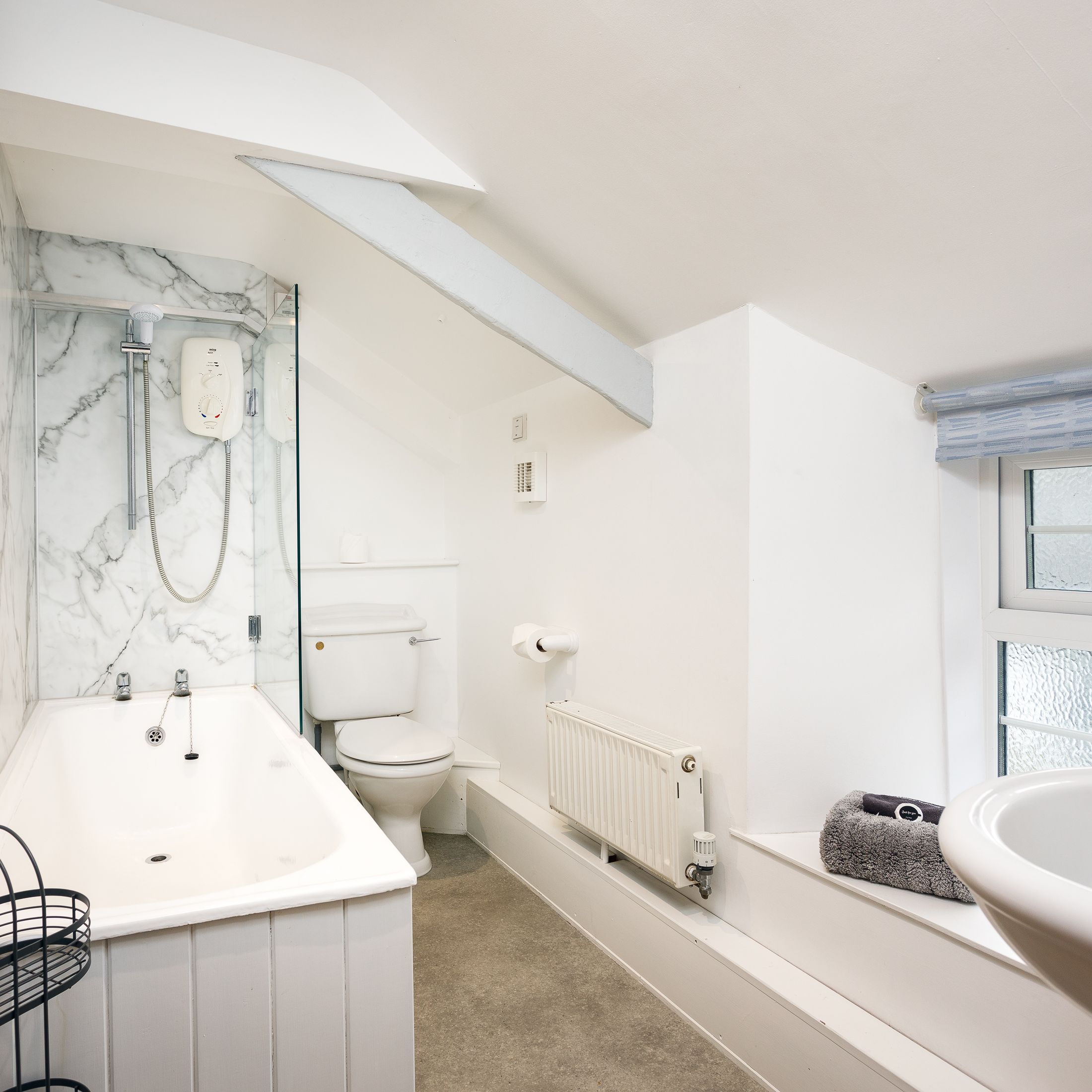 Bright bathroom with a bathtub, shower, toilet, window, and wooden door