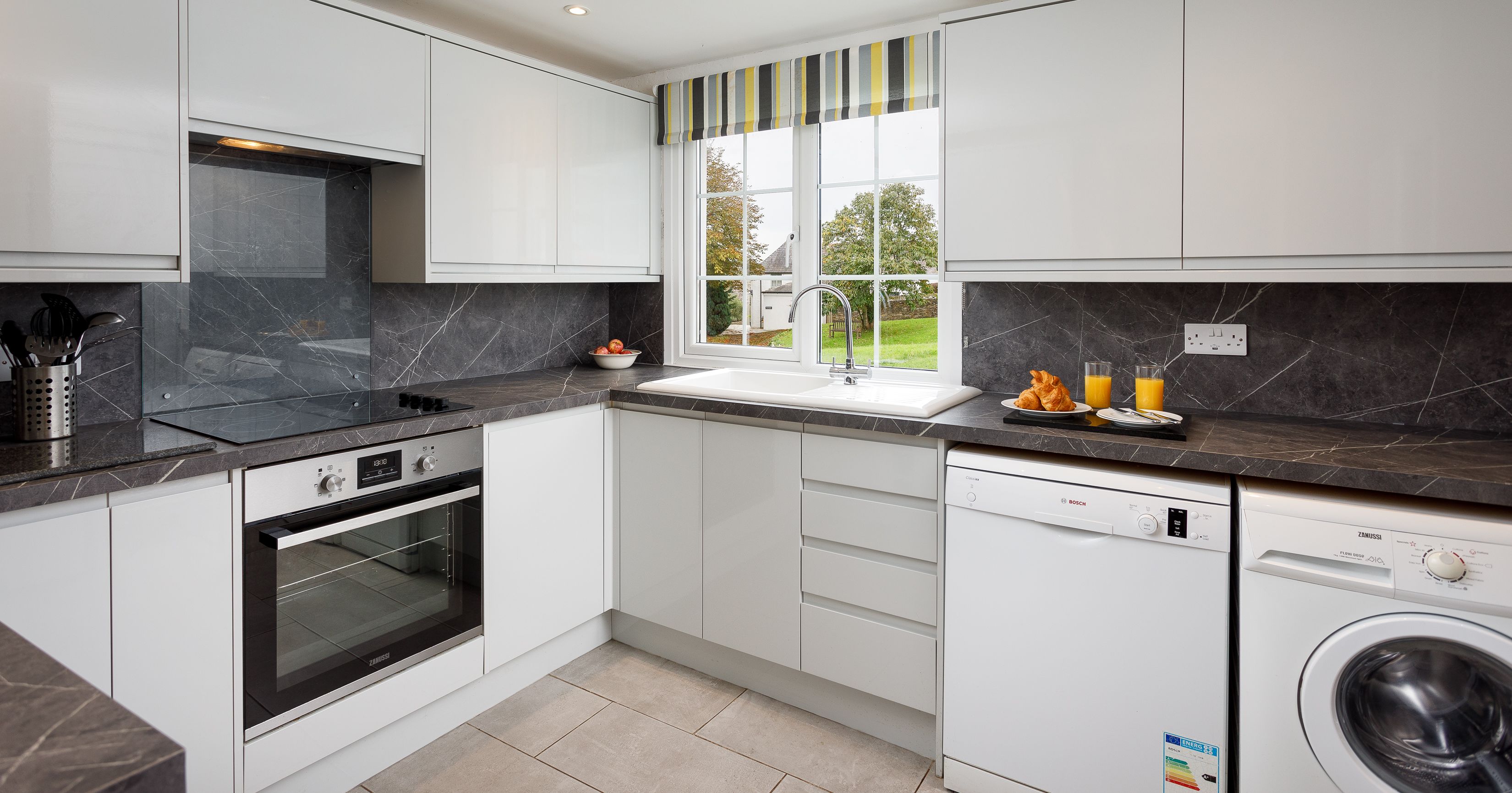 Modern kitchen with white cabinets, marble countertops, and appliances including an oven, dishwasher, and washing machine.