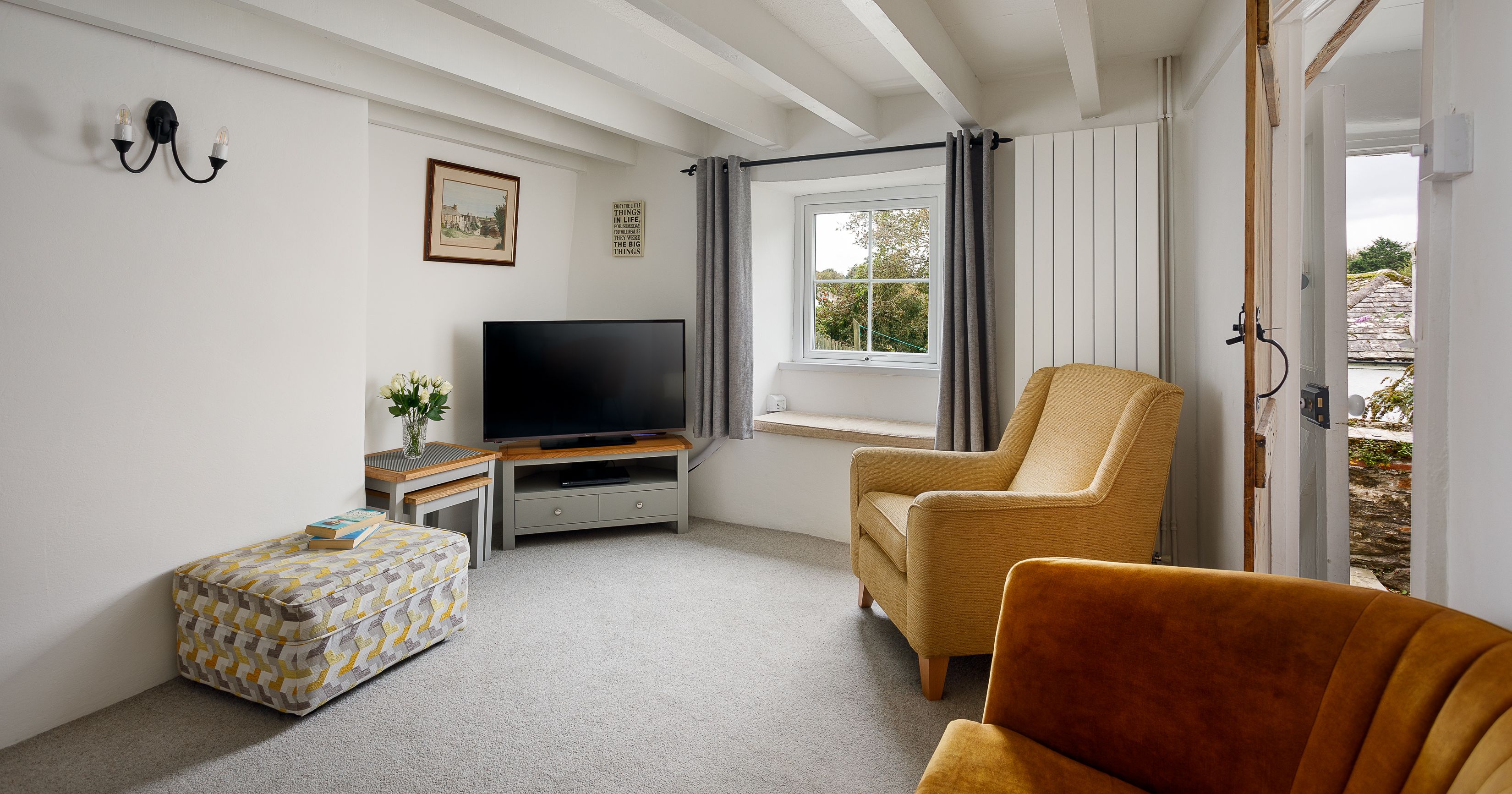 Cozy living room with mustard armchairs, patterned ottoman, TV, and window with outside view.