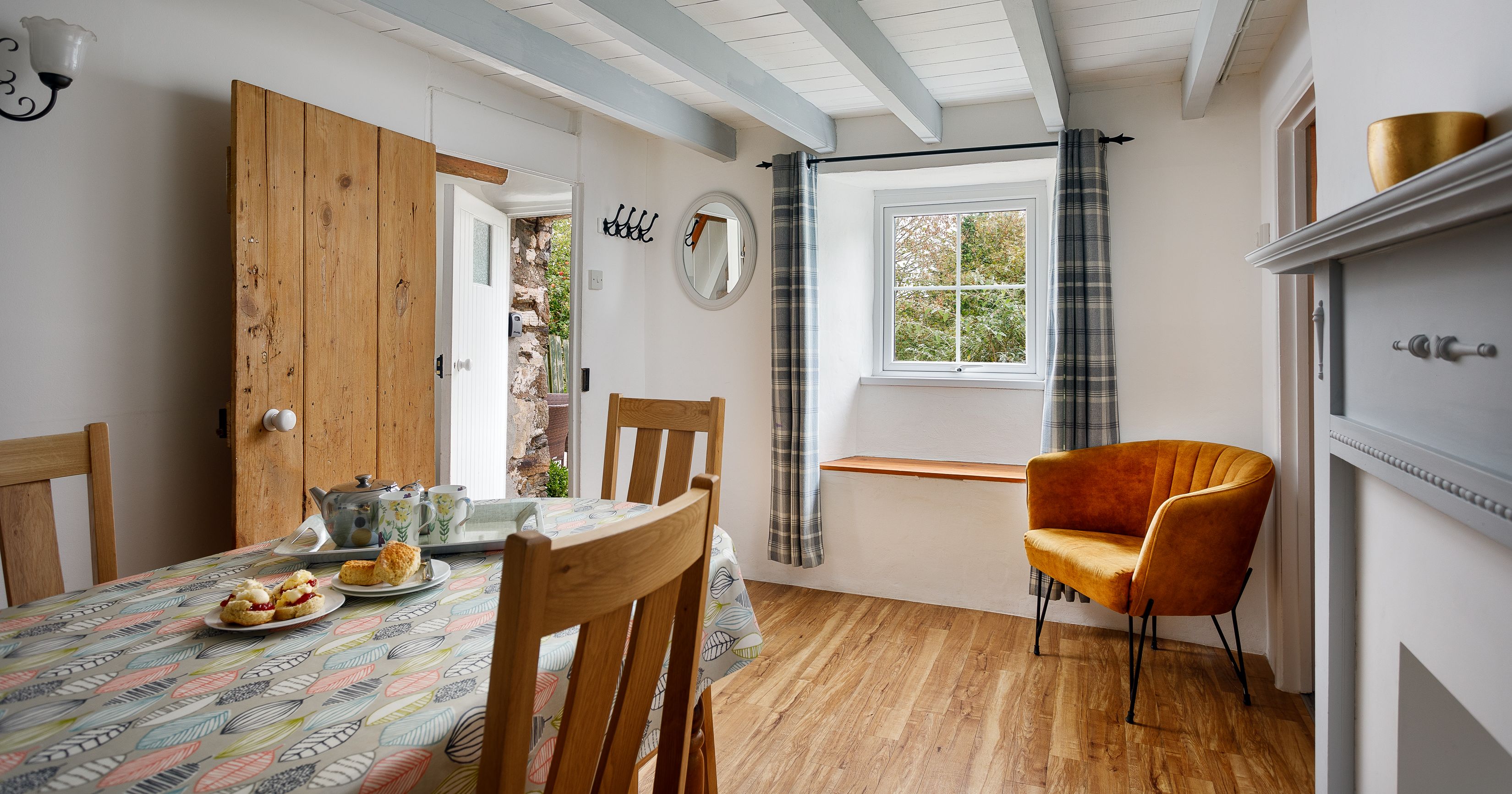 Cozy dining room with wooden floor, patterned tablecloth, tea set, and yellow armchair near a window