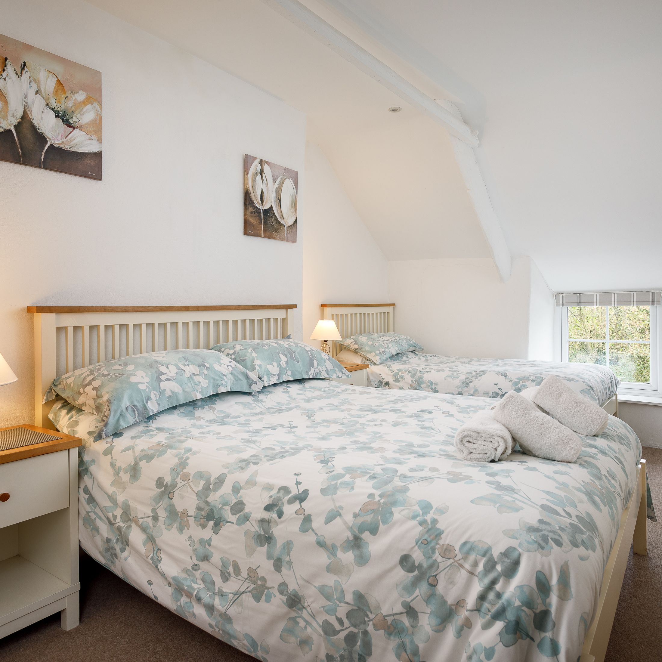 Cozy twin bedroom with floral bedding, bedside tables, and soft lighting.