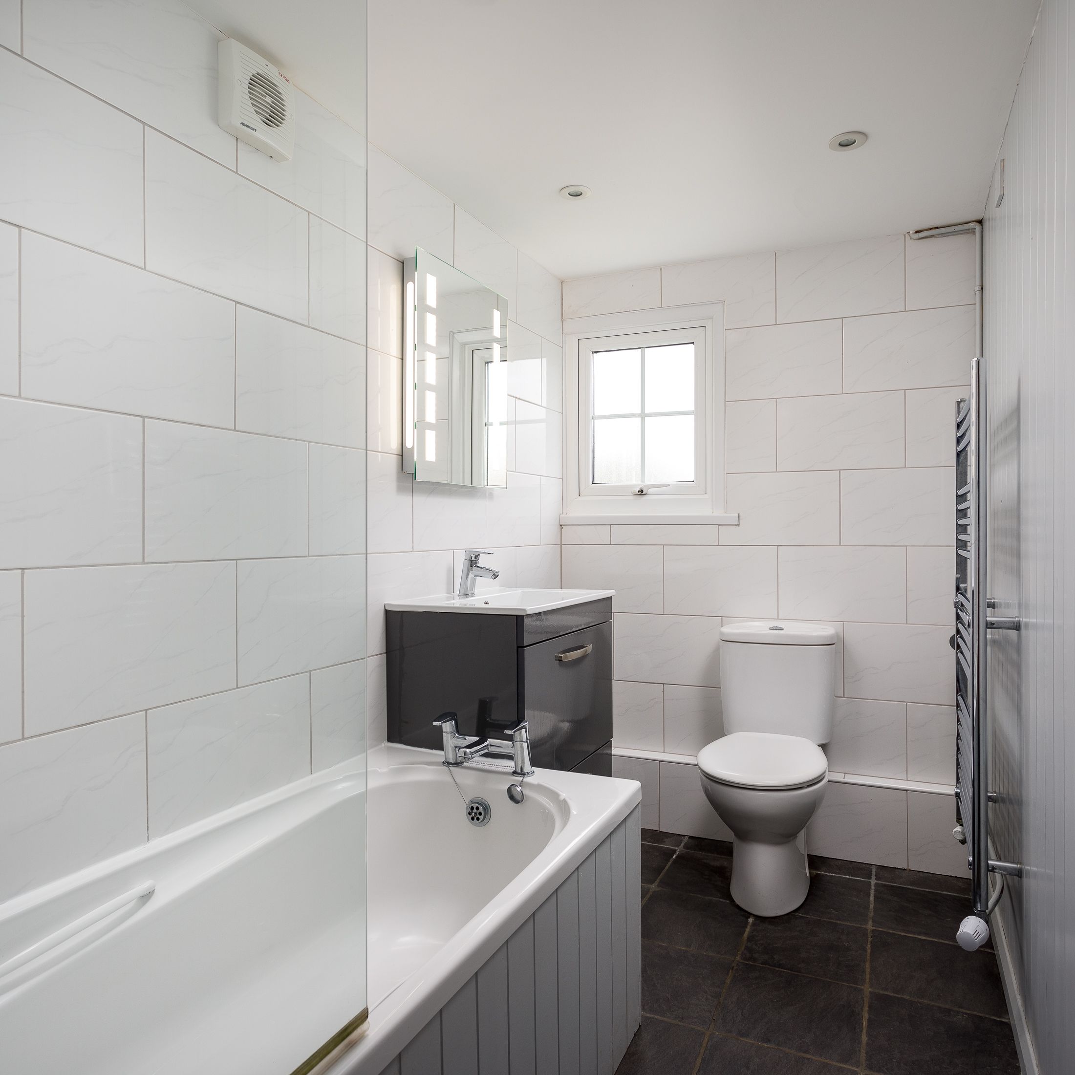 Modern bathroom with bathtub, toilet, sink and grey vanity unit
