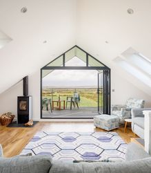 Modern attic living room with large glass doors opening to a balcony overlooking green fields.