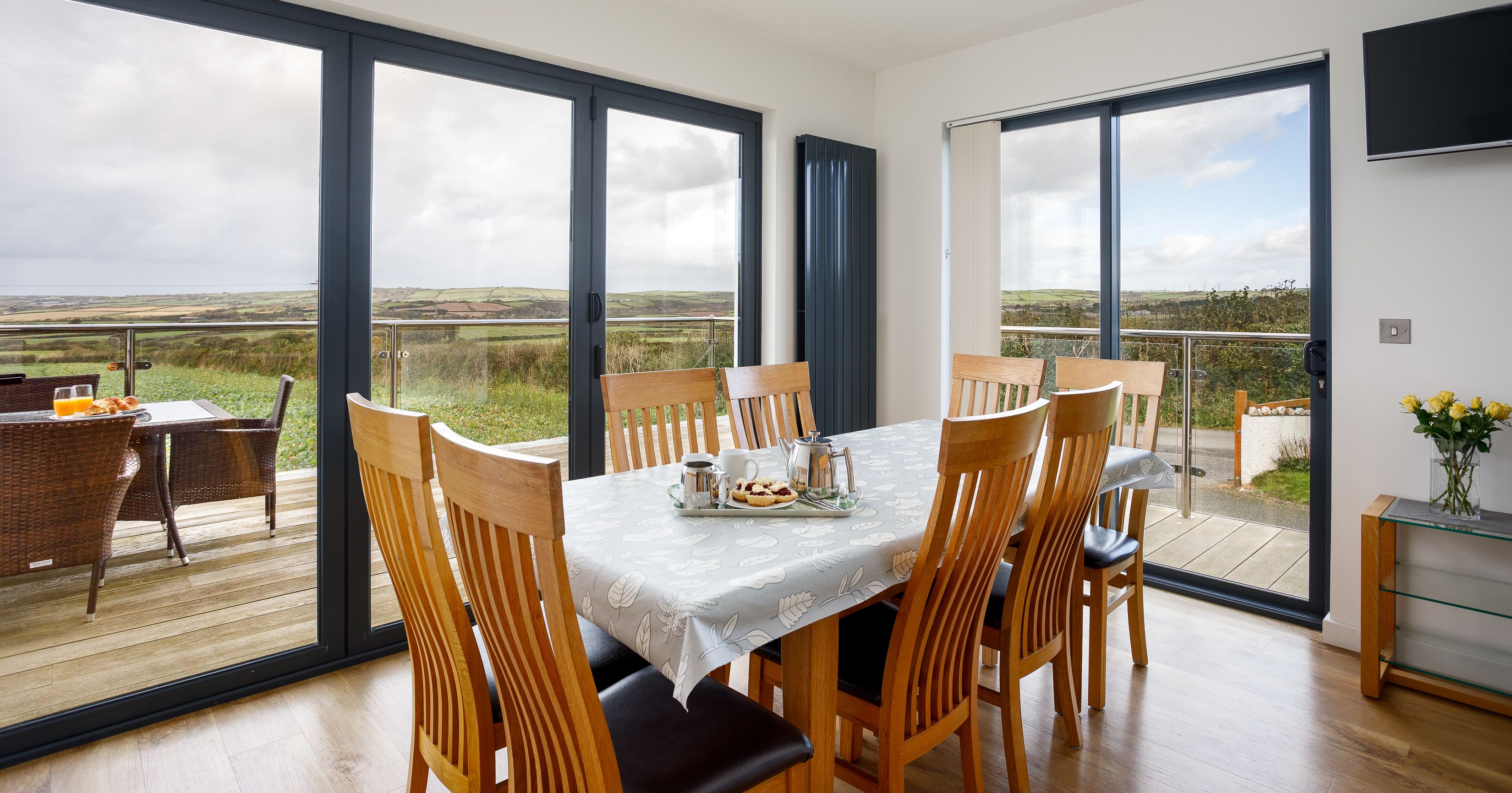 Modern dining room with large windows overlooking countryside and outdoor patio.