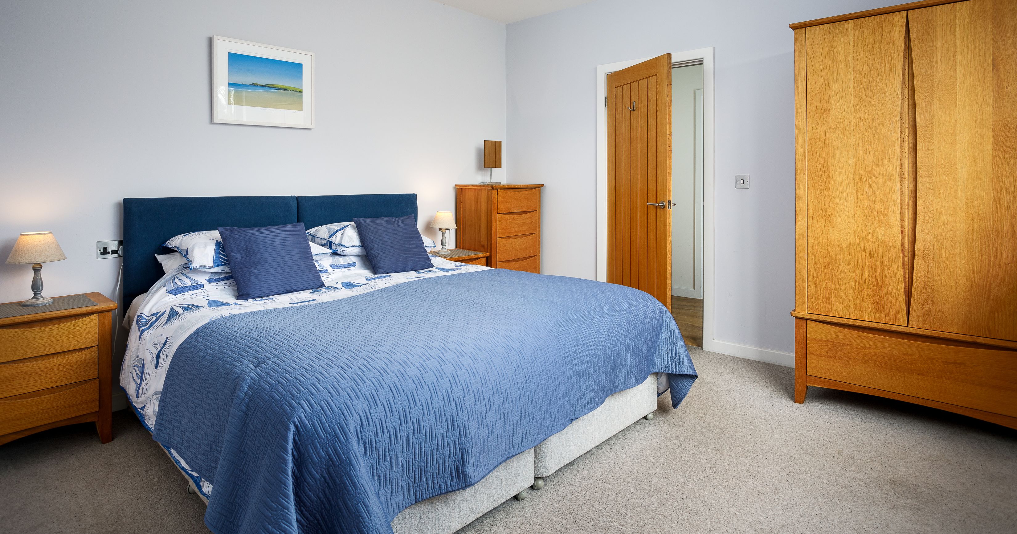 A cozy bedroom with a double bed covered in blue bedding, featuring wooden furniture and soft lighting.