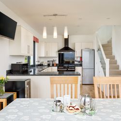 Modern kitchen and dining area with staircase, set table with scones and tea, and white cabinets.