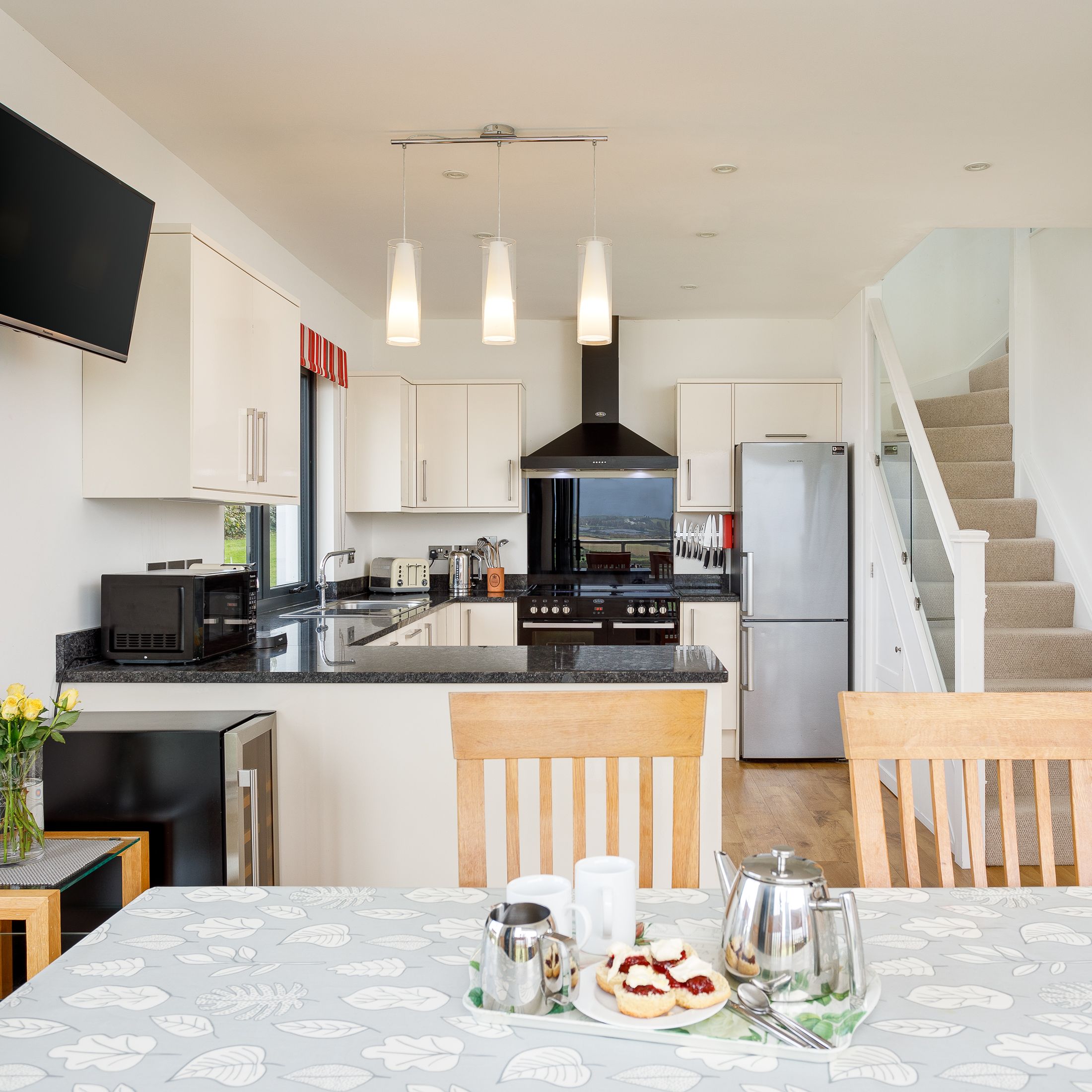 Modern kitchen and dining area with staircase, set table with scones and tea, and white cabinets.