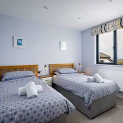 Twin bedroom with two single beds, blue geometric bedding, bedside tables with lamps, and a window offering a scenic view.