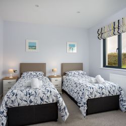 Modern twin bedroom with two single beds, floral bedding, bedside tables with lamps, and a large window with a striped valance.
