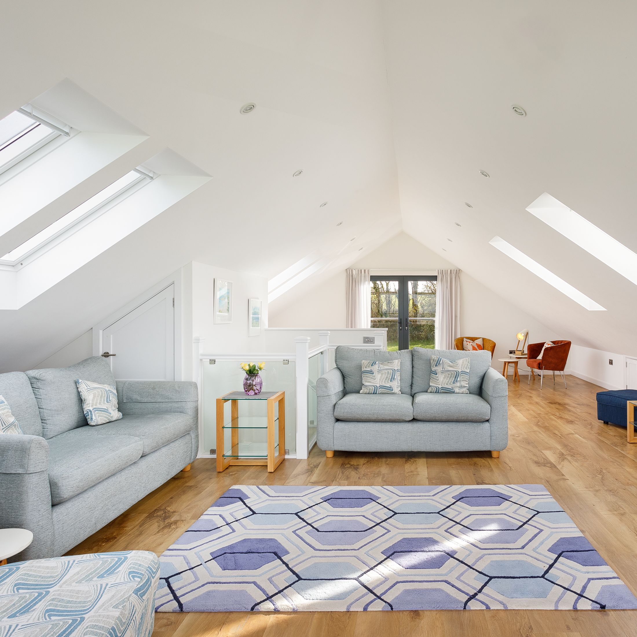 Bright and spacious loft living room with modern furniture, wooden floors, skylights, and cozy seating area.