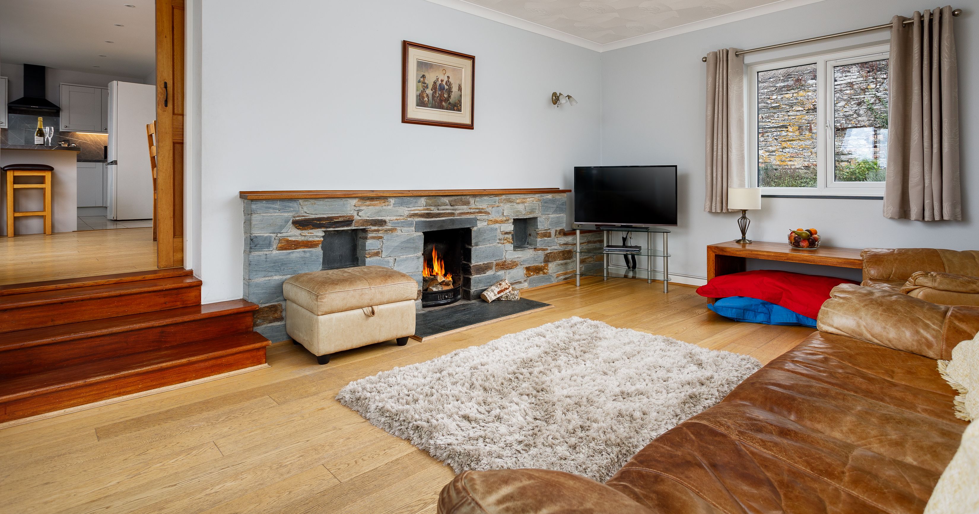 Cozy living room with fireplace, TV, and modern decor leading into a bright kitchen