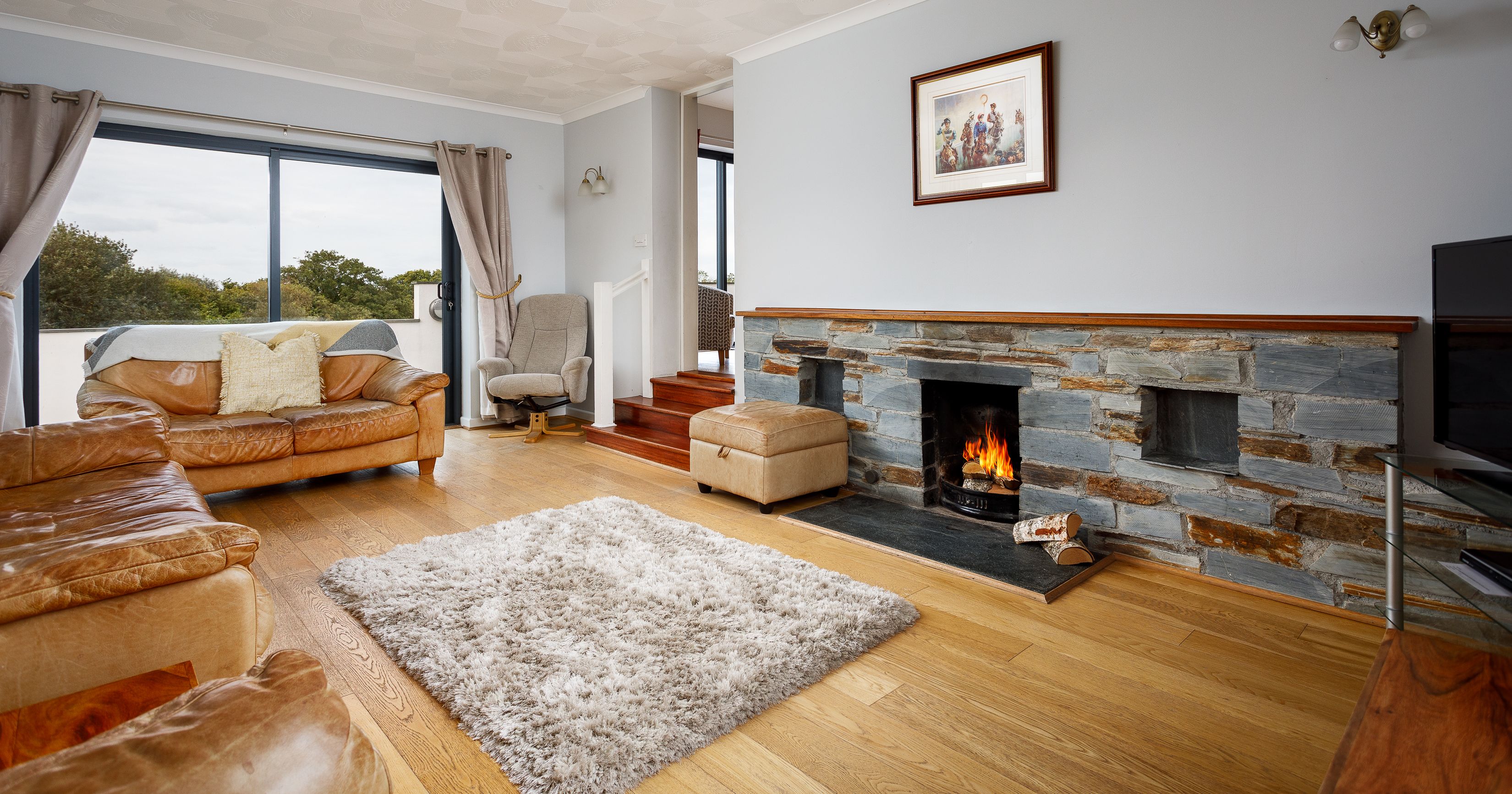 Cozy living room with leather sofas, stone fireplace, and large window with countryside view