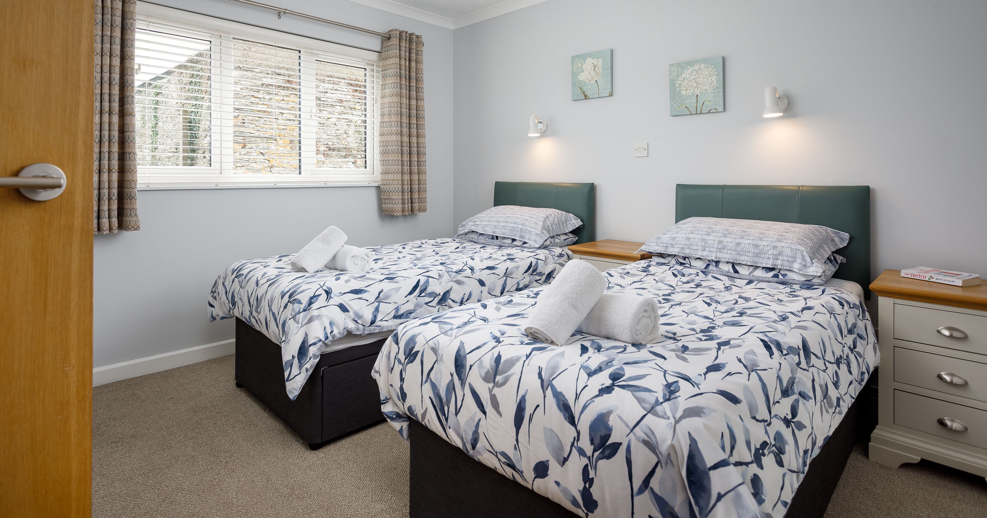 Twin bedroom with two single beds, patterned bedding, and rolled towels on each bed.