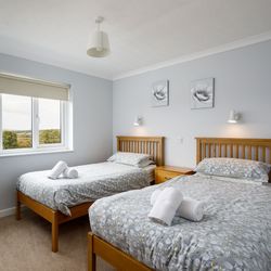 Twin bedroom with wooden beds, grey floral bedding, bedside table, and a large window with countryside view.