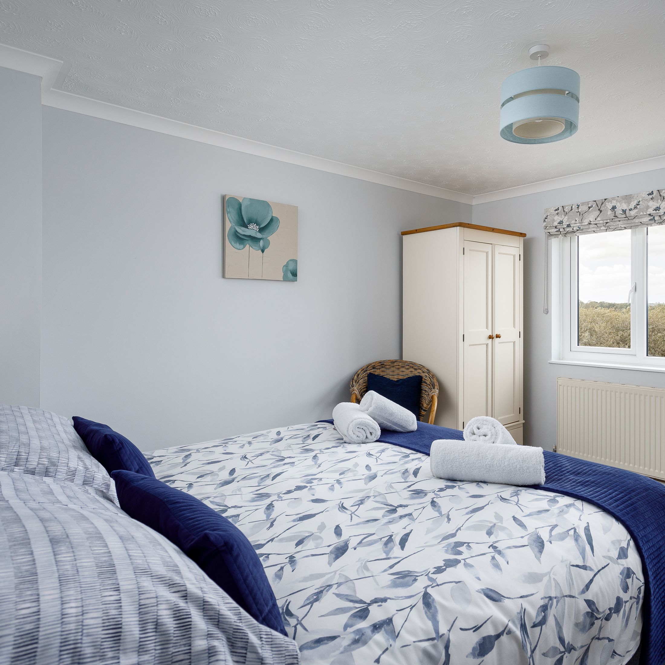 Cozy bedroom with double bed, floral bedding, window with nature view, and wardrobe.