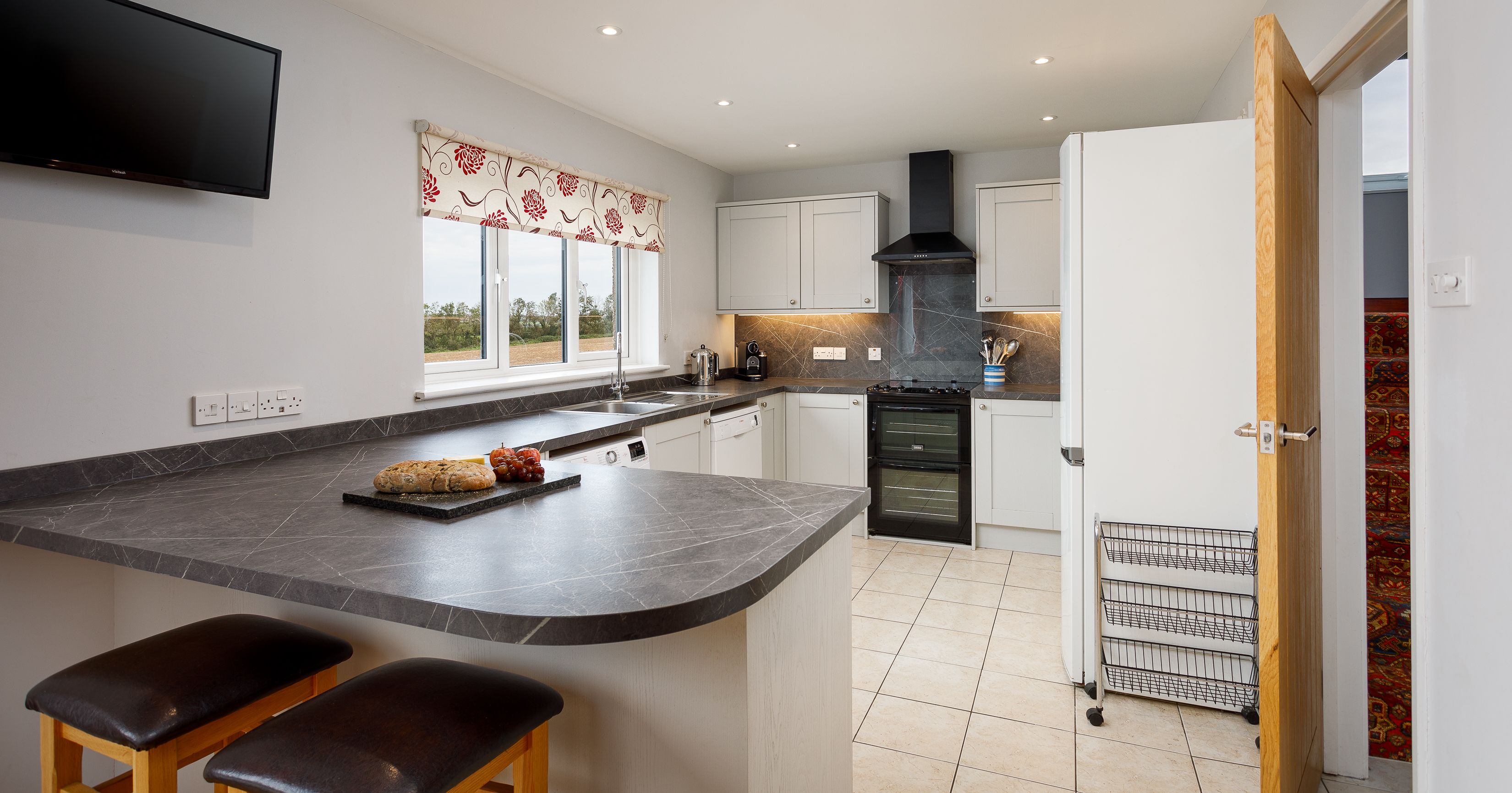 Modern kitchen with breakfast bar, two stools, and a wall-mounted TV