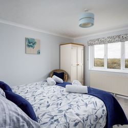 Bright and cozy bedroom with a double bed, floral bedding, wardrobe, and large window overlooking greenery.