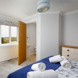 Bright bedroom with large window, double bed with blue accents, and towels neatly arranged.
