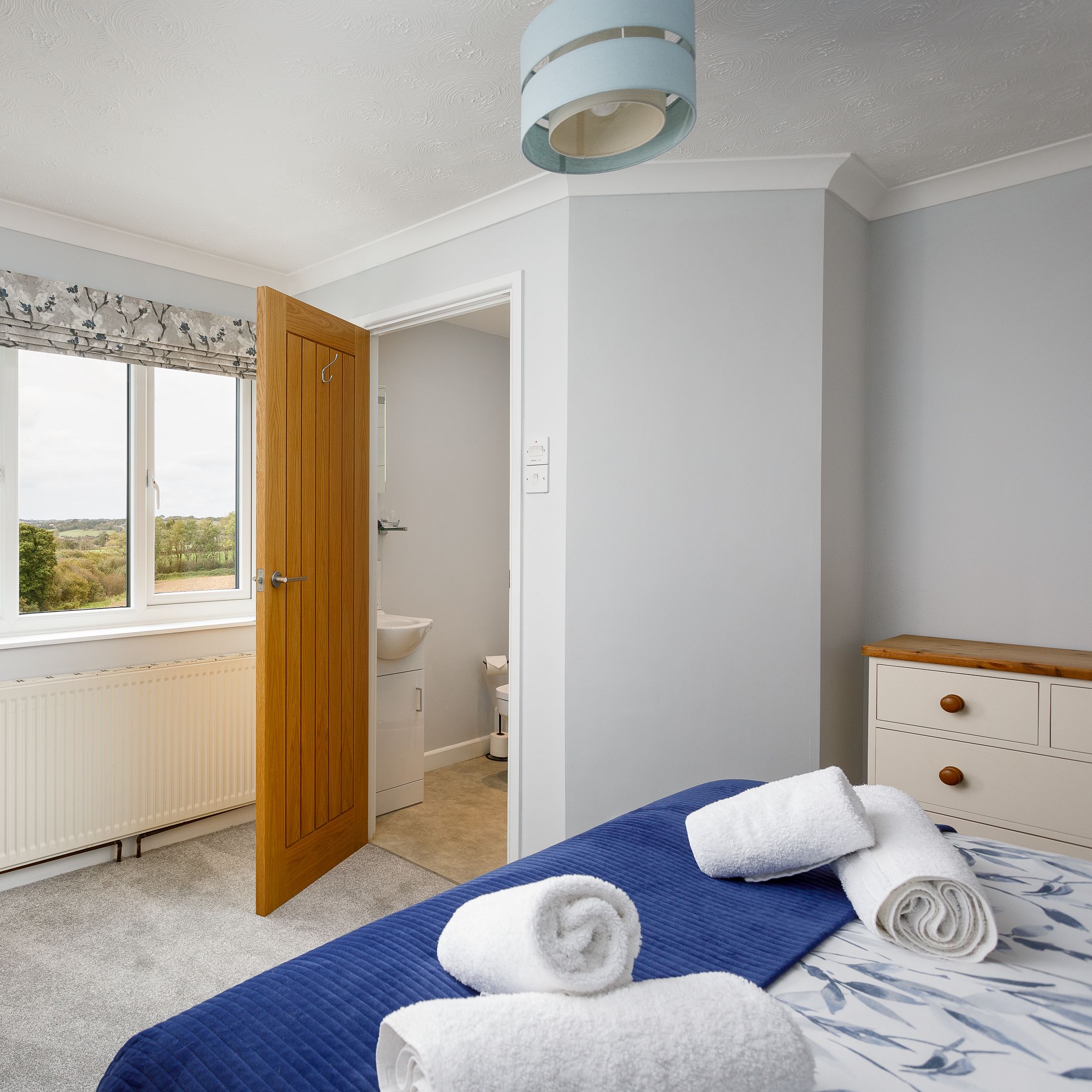 Bright bedroom with large window, double bed with blue accents, and towels neatly arranged.
