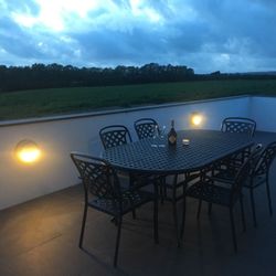 Outdoor patio table with chairs, wine bottle, glasses, and candle at dusk overlooking fields