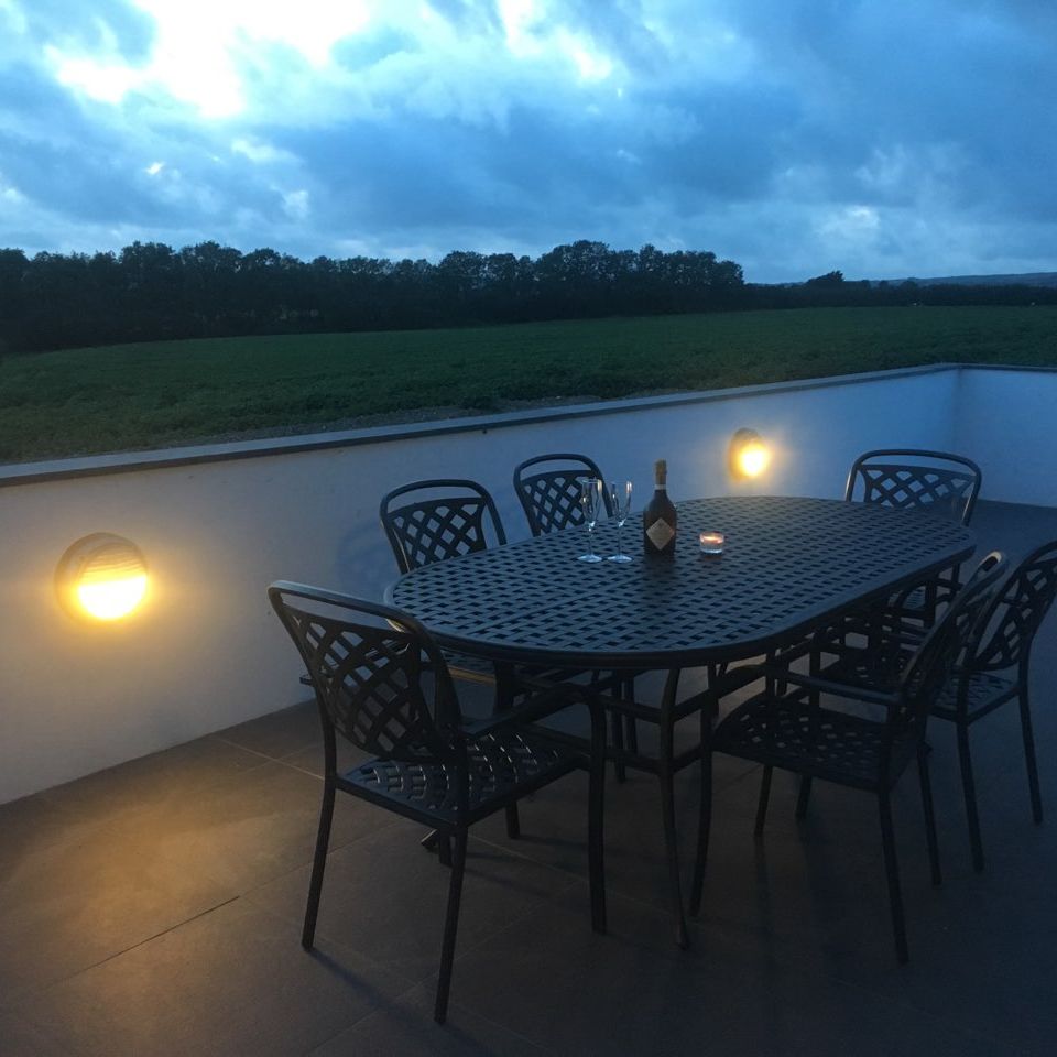 Outdoor patio table with chairs, wine bottle, glasses, and candle at dusk overlooking fields
