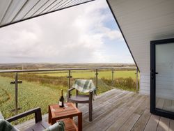 Balcony with two chairs, a small table with wine, overlooking green fields and hills.