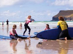 Kids in wetsuits taking a surf lesson on the beach with a surf instructor.