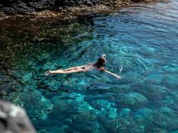 Person swimming in clear blue natural pool surrounded by rocky cliffs.