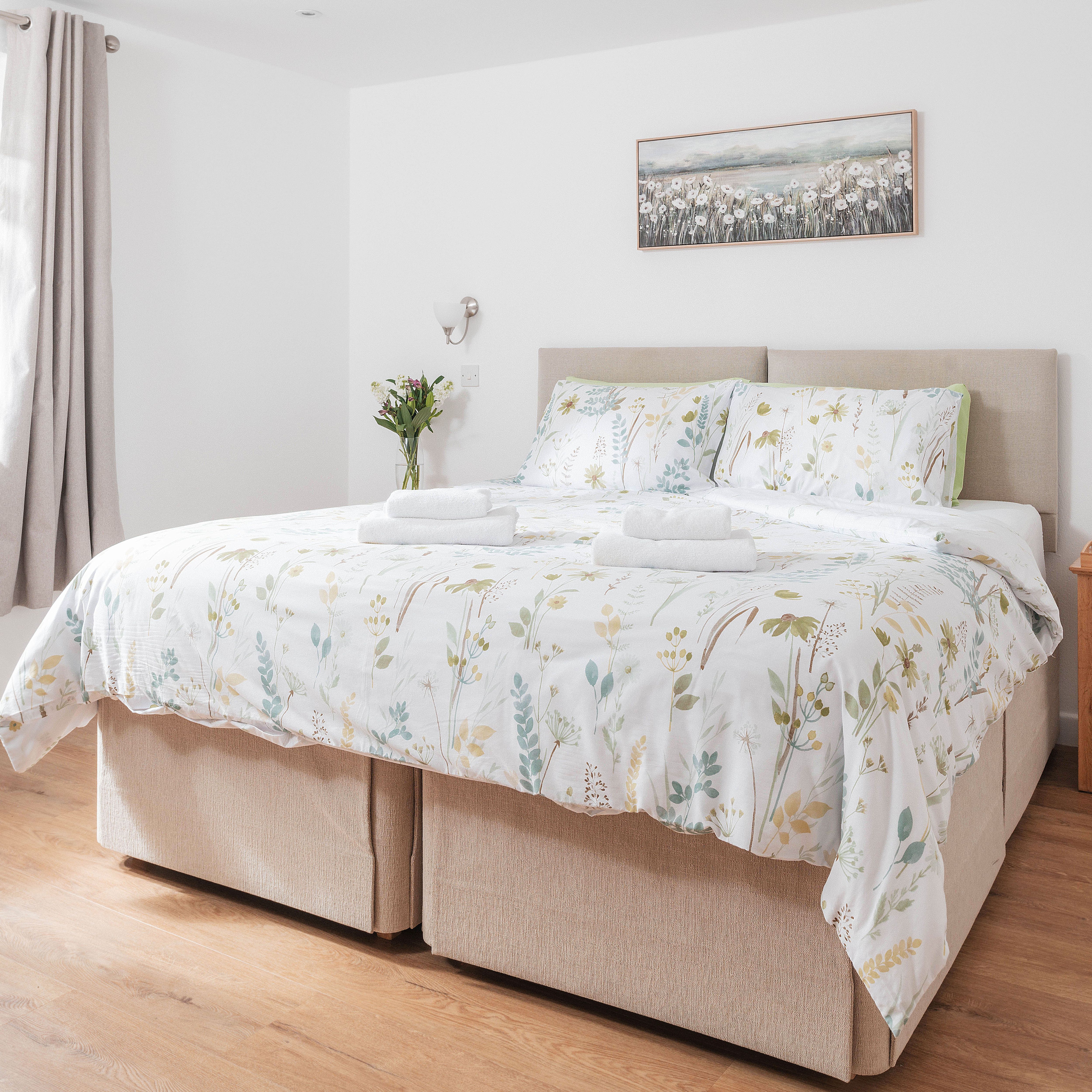 Bright bedroom with a double bed, floral bedding, bedside table, and window.