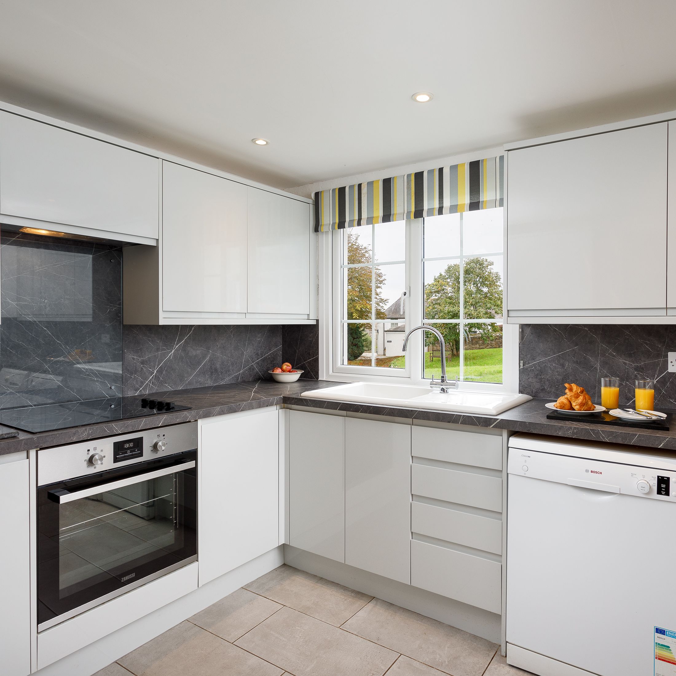 Modern kitchen with white cabinets, grey countertops, and a window overlooking a garden