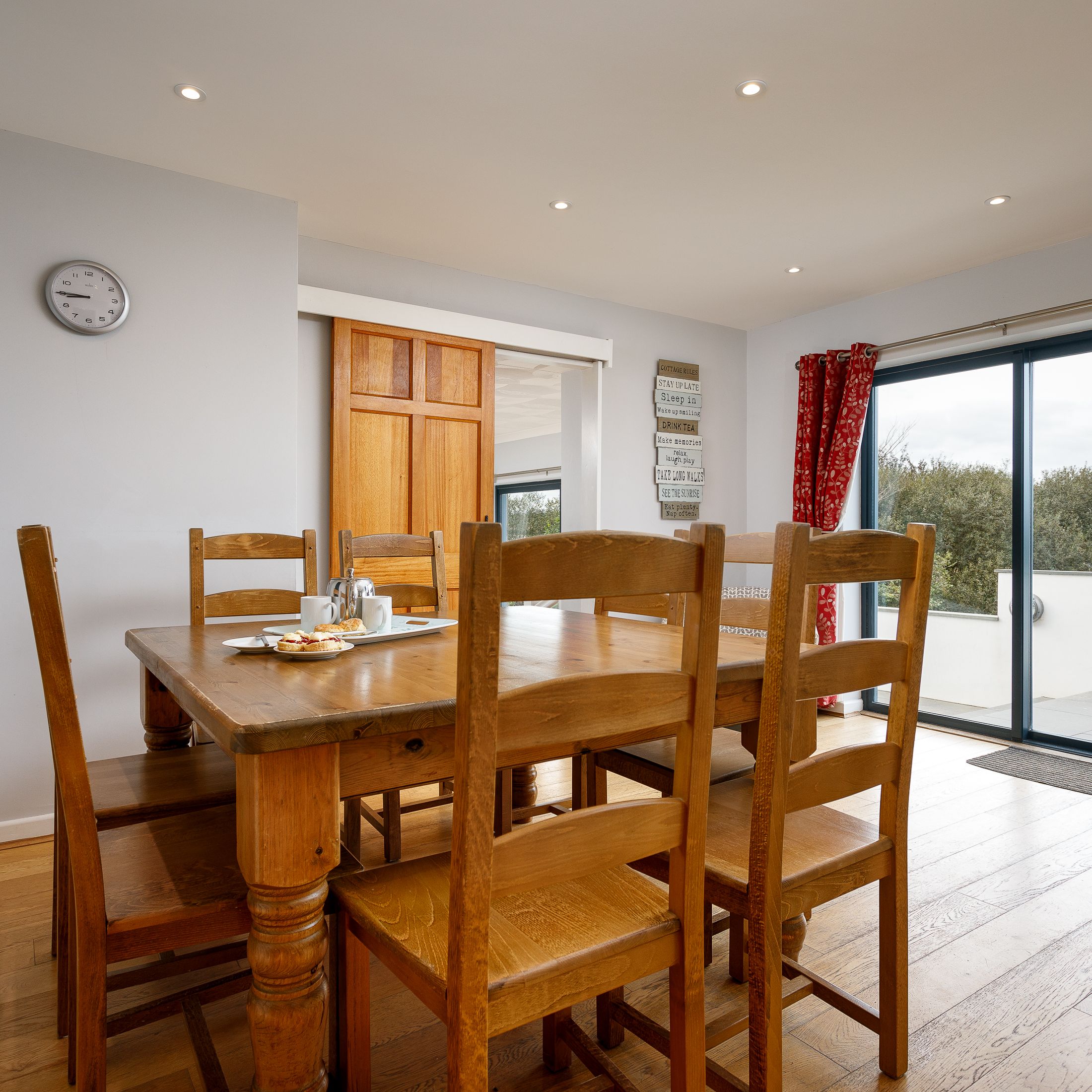 Dining area with wooden table and chairs, sliding glass doors with red curtains, and a view outside