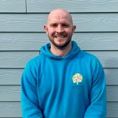 Smiling person in a blue hoodie standing in front of a light blue wooden wall