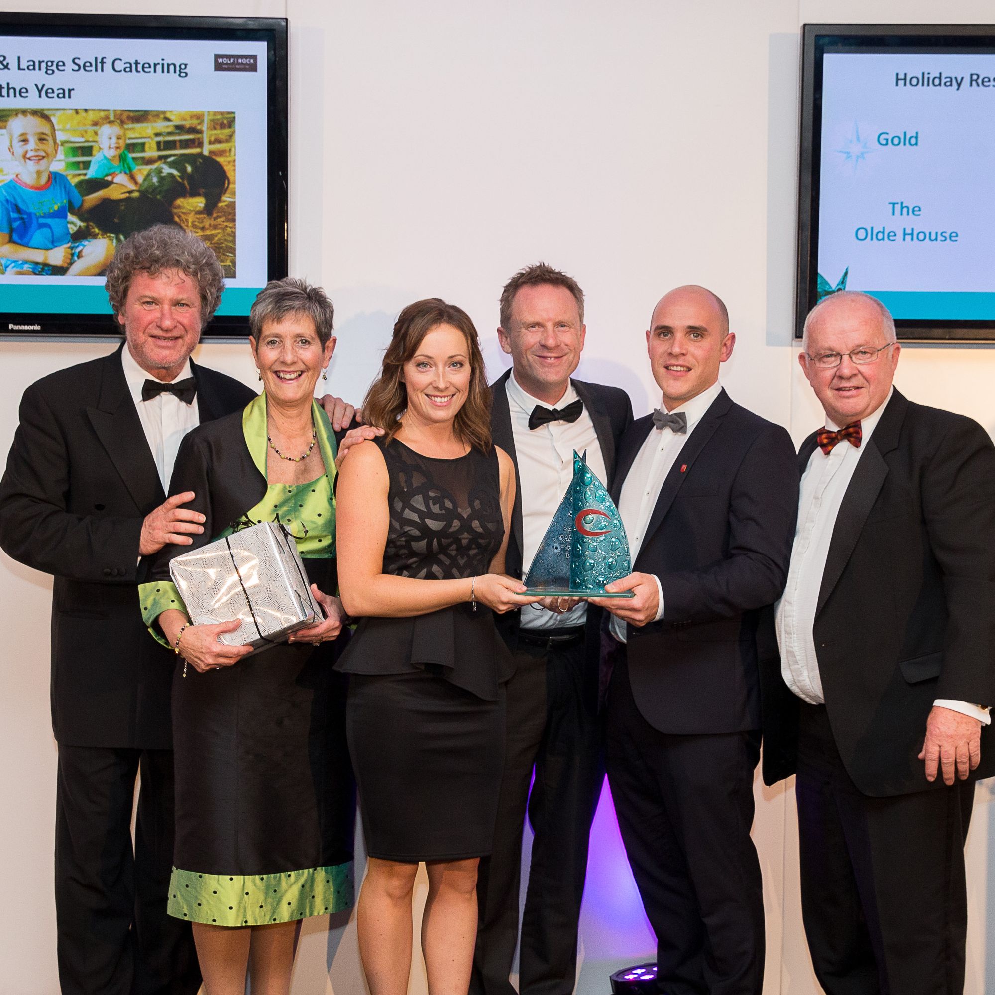 Group of people receiving tourism awards at an event, with Cornwall Tourism Awards 2015/16 Gold and South West England Tourism Excellence Awards 2015-2016 Gold logos displayed.