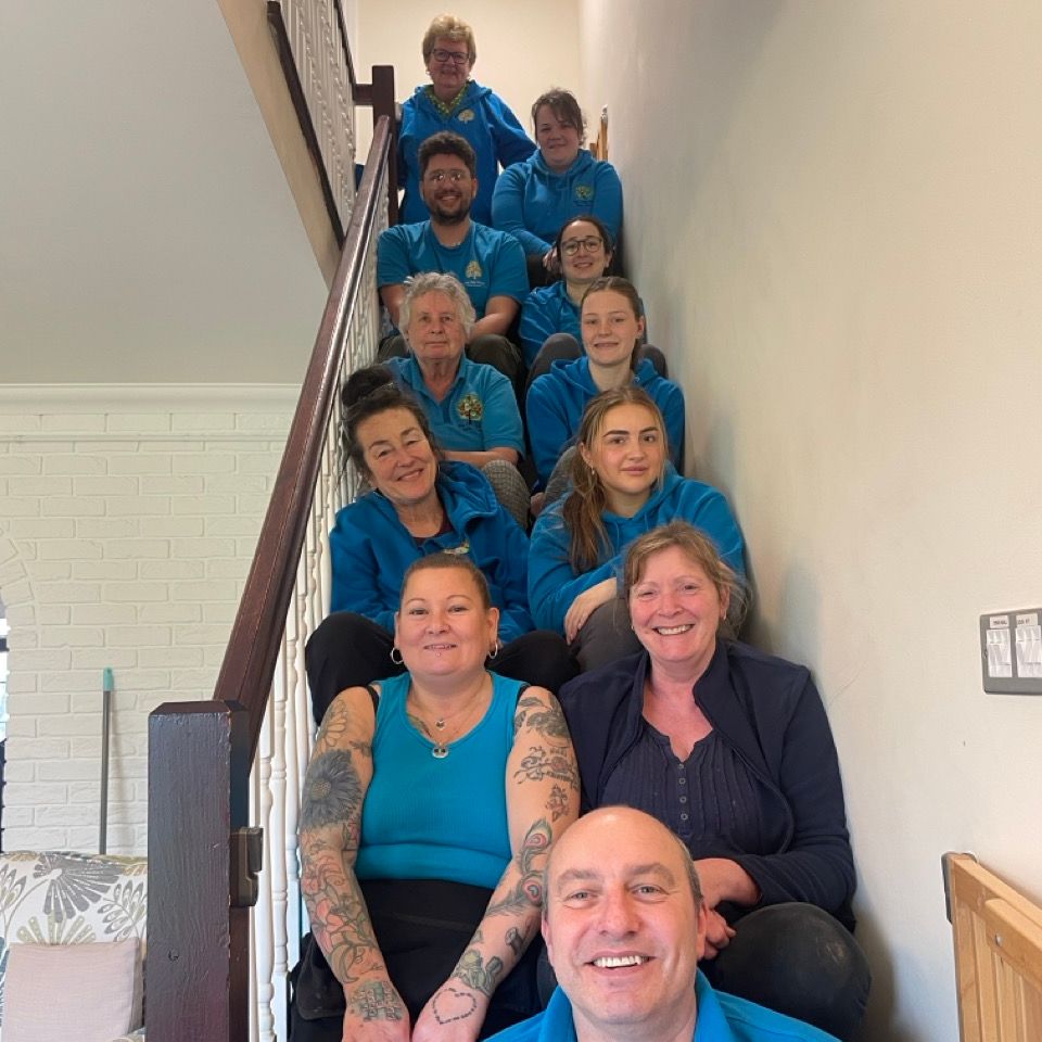 Group of people sitting on a staircase, posing and smiling for a photo, all wearing blue tops.