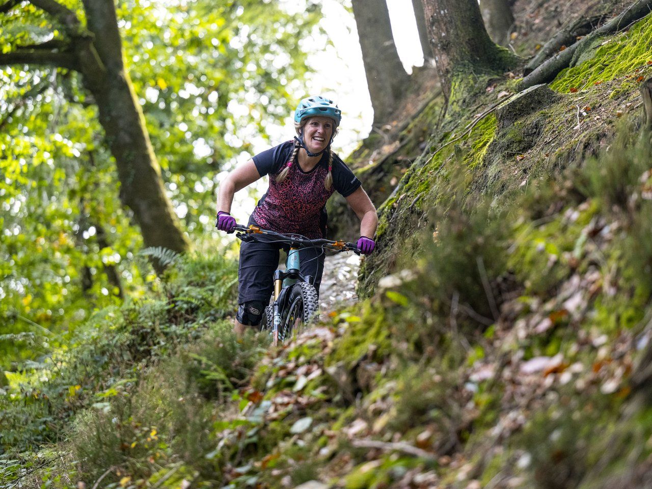 Person mountain biking down a forest trail with greenery and moss-covered ground.