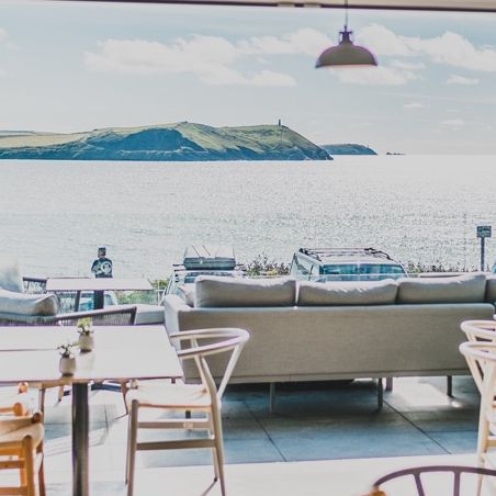 Modern cafe interior with open doors leading to a scenic view of the ocean and a green hill across the water.