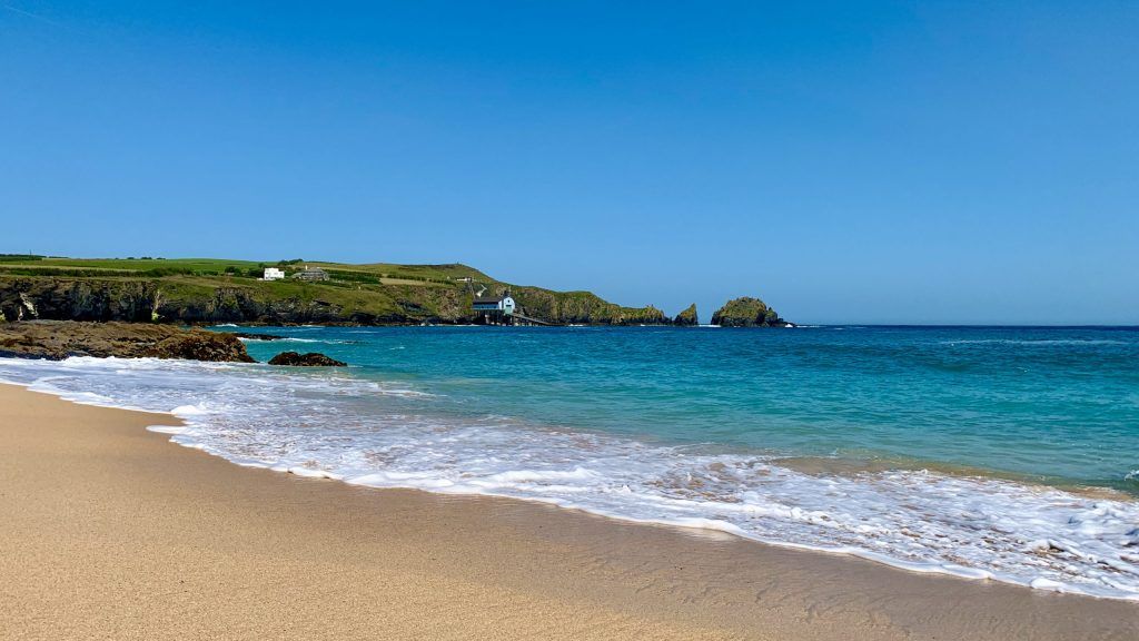 Sandy beach with turquoise water and green cliffs under a clear blue sky