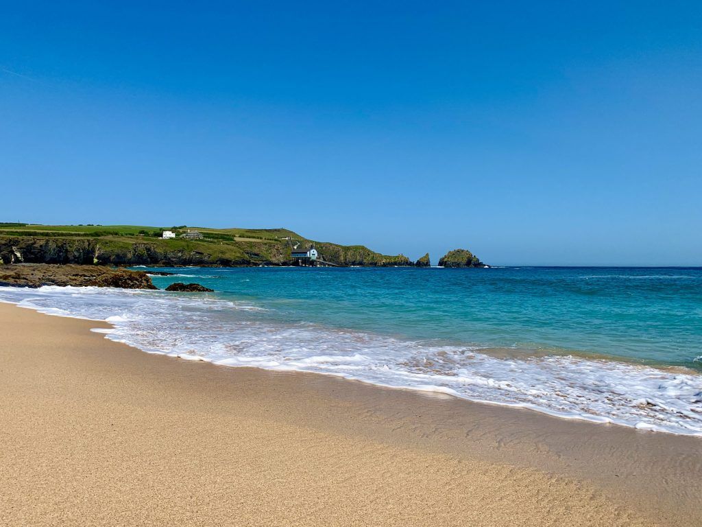 Sandy beach with turquoise water and green cliffs under a clear blue sky