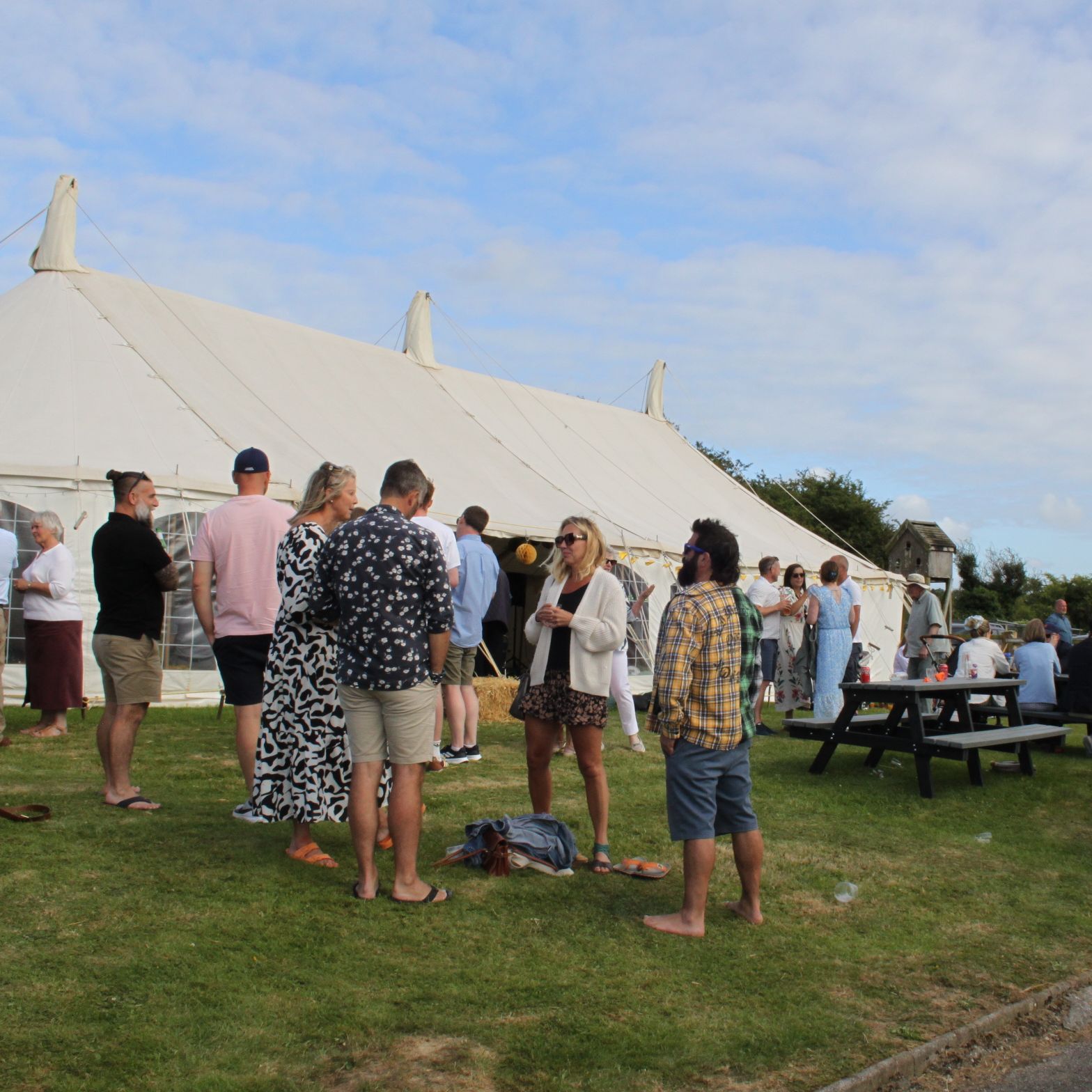 Group of people socializing outside a large white tent at an outdoor event.