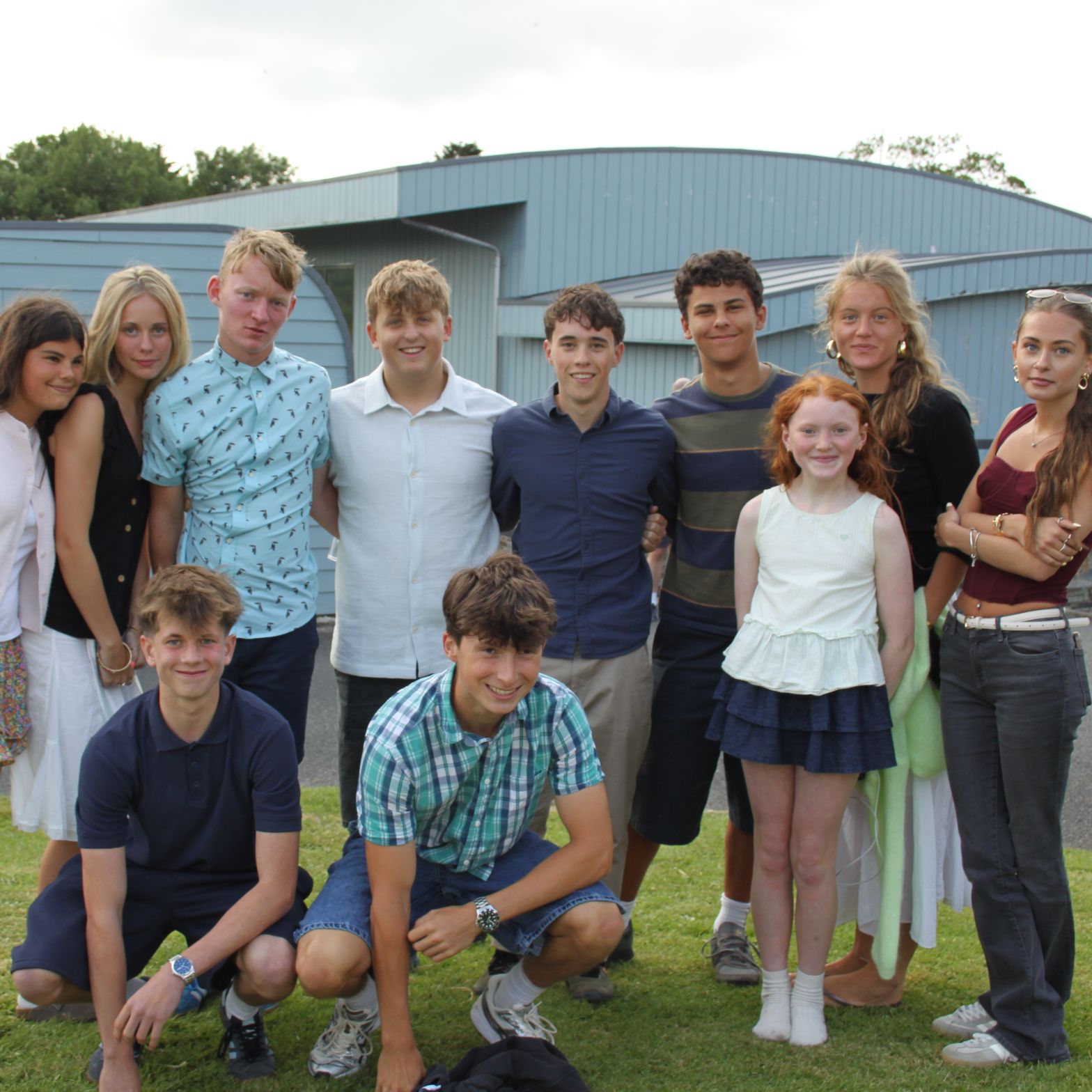 A group of young people posing together outdoors in front of modern blue buildings.