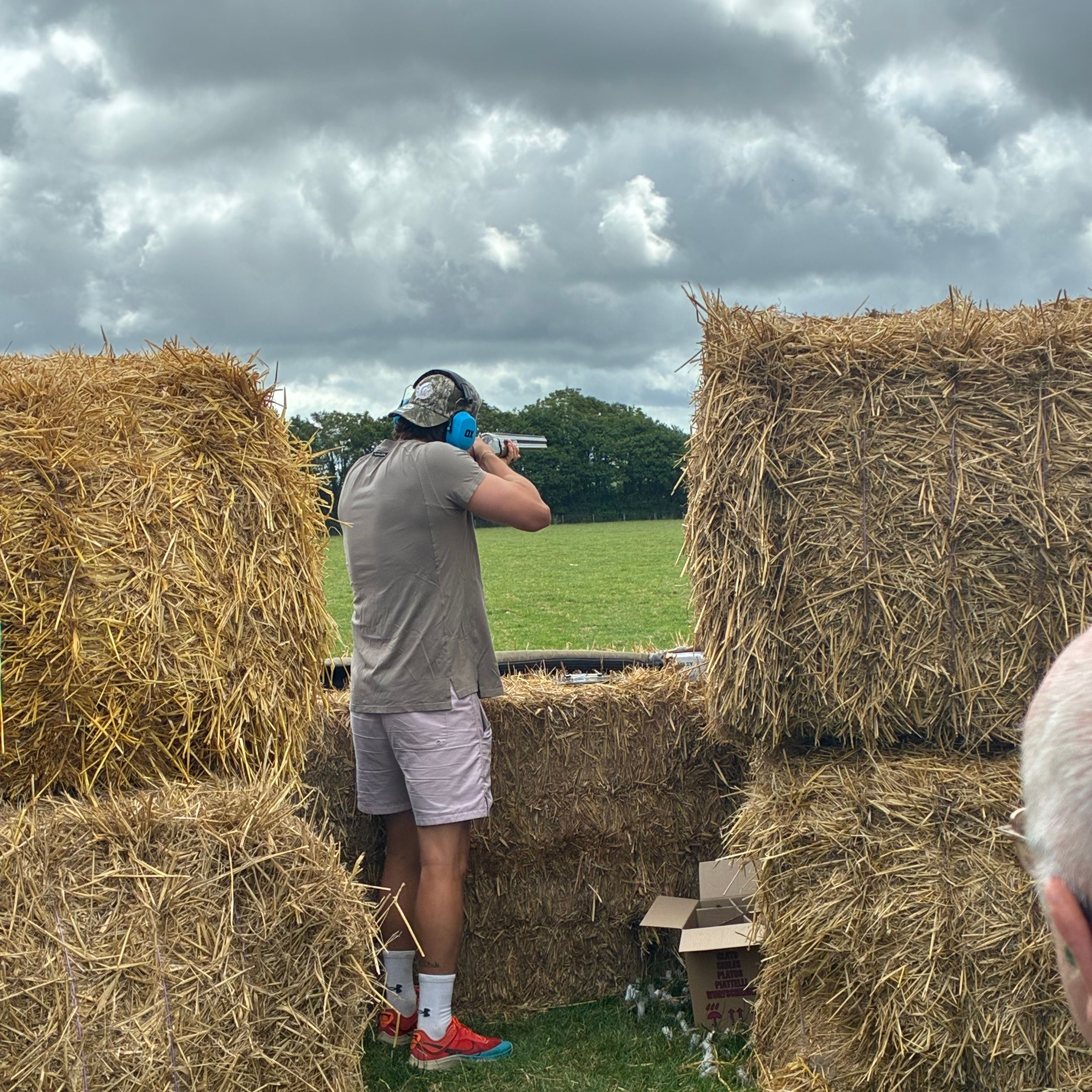 Person aiming a shotgun between hay bales on a cloudy day