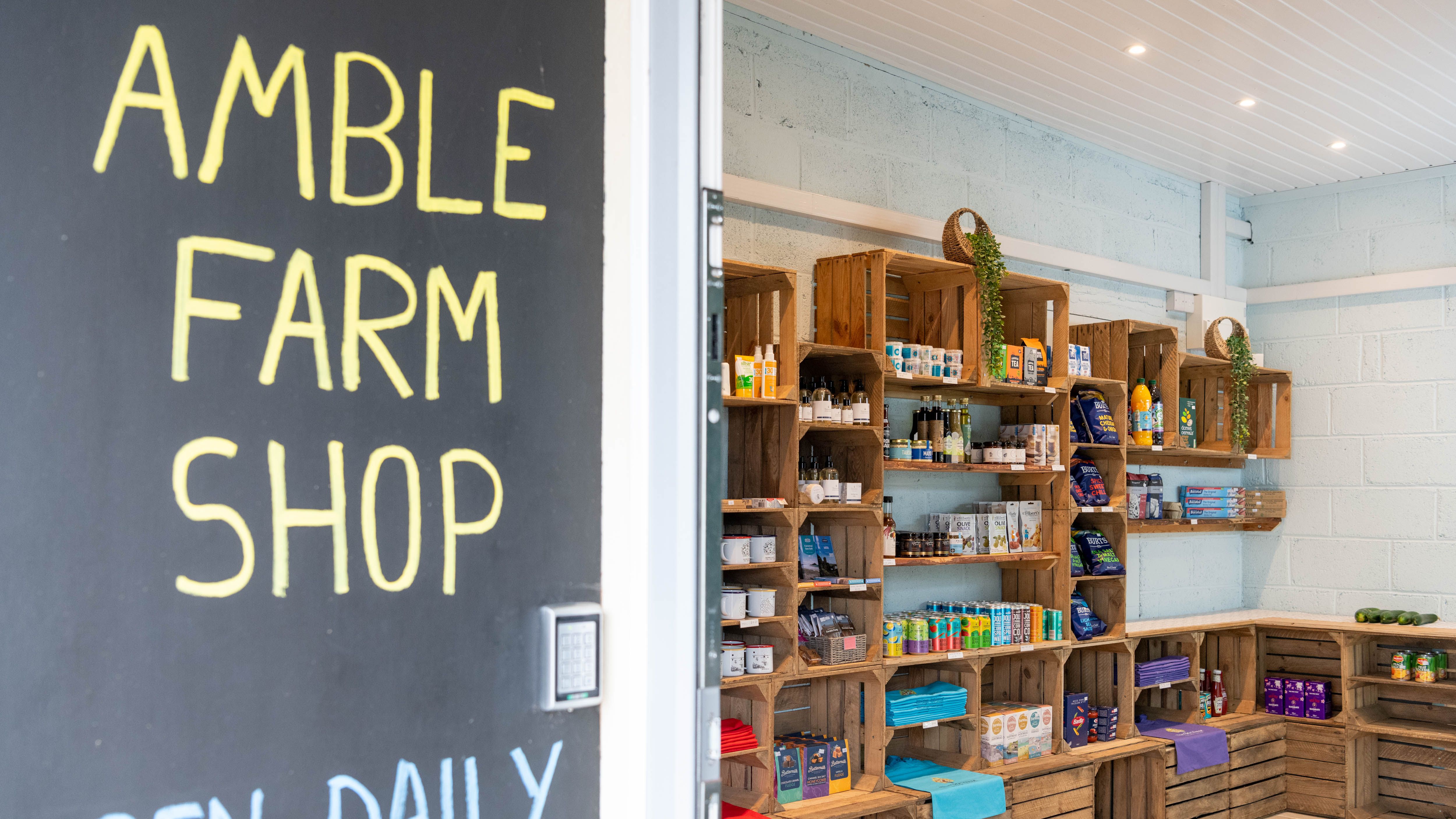 Entrance to Amble Farm Shop with a chalkboard sign reading 'AMBLE FARM SHOP OPEN DAILY' and shelves inside displaying various local products.
